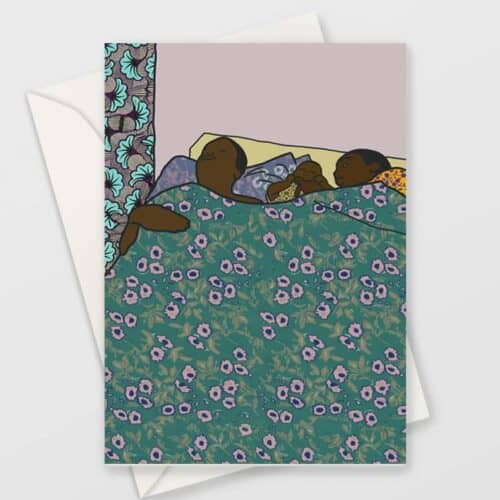 Greeting card with an illustration of two black people and their baby in bed. The mother holds the baby's hand. Has a teal and pink floral pattern on the blanket. The background is a light purple colour. The card is inside a white envelope.